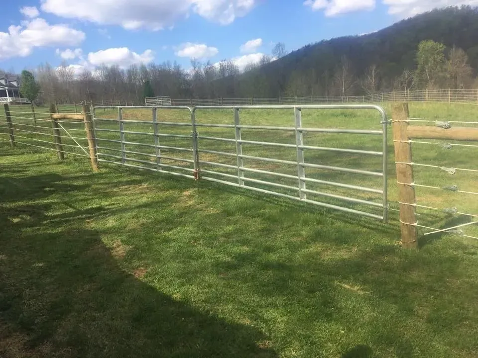 Metal farm gate and wire fence in a grassy field under a blue sky