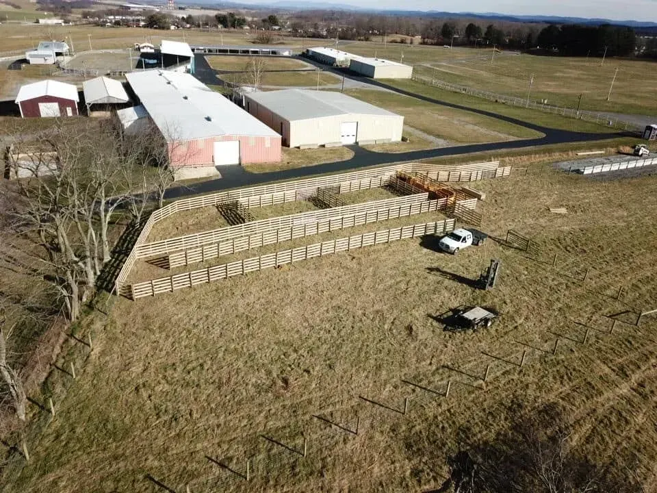 Aerial view of a farm with long barns, hay bales, and a few horses in a grassy field