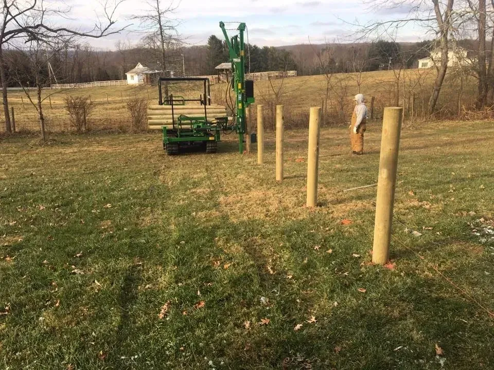 Fence posts in a grassy field with a green drilling machine in the background