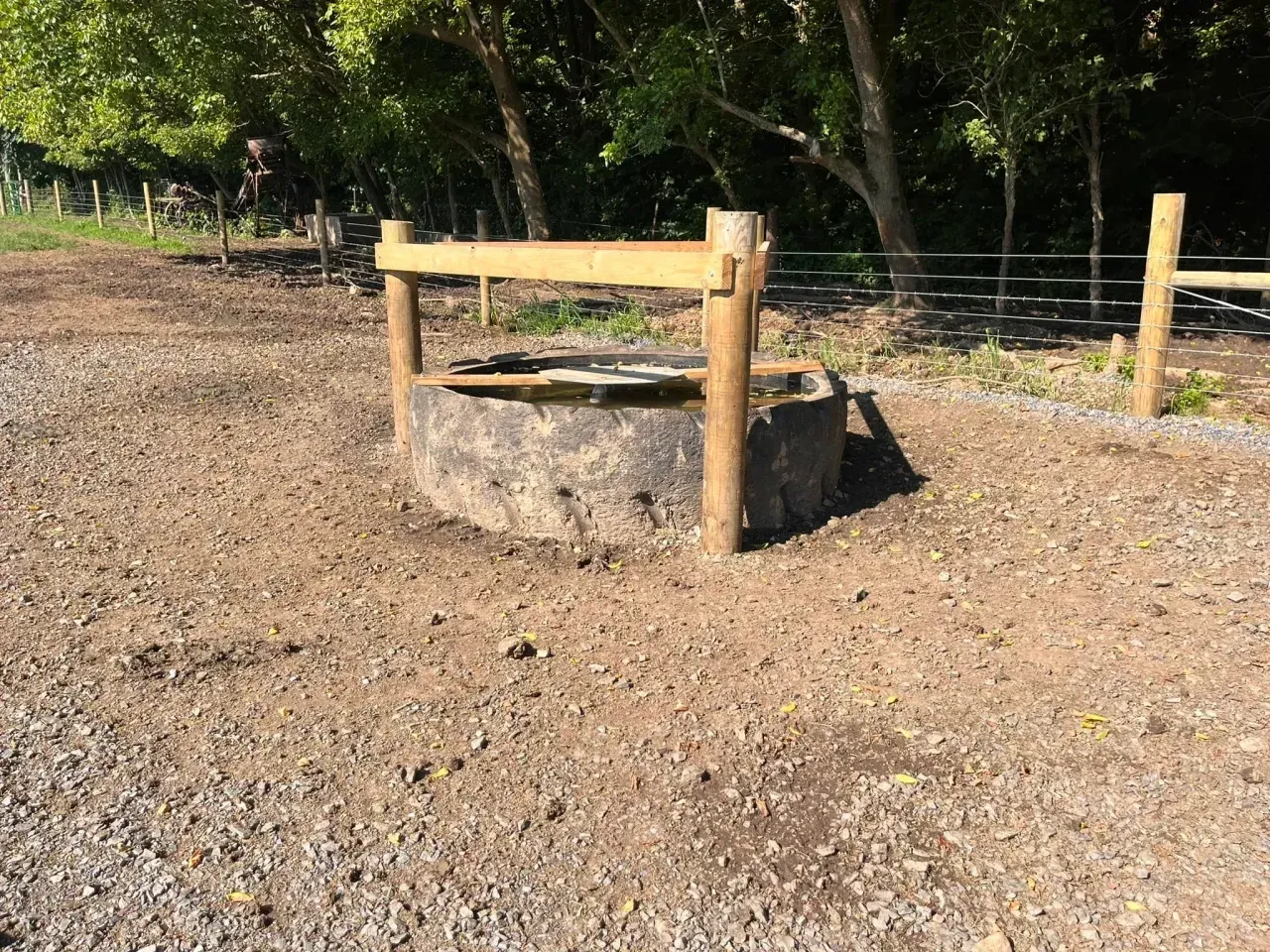 Stone fire pit surrounded by wooden posts in a gravel clearing near trees