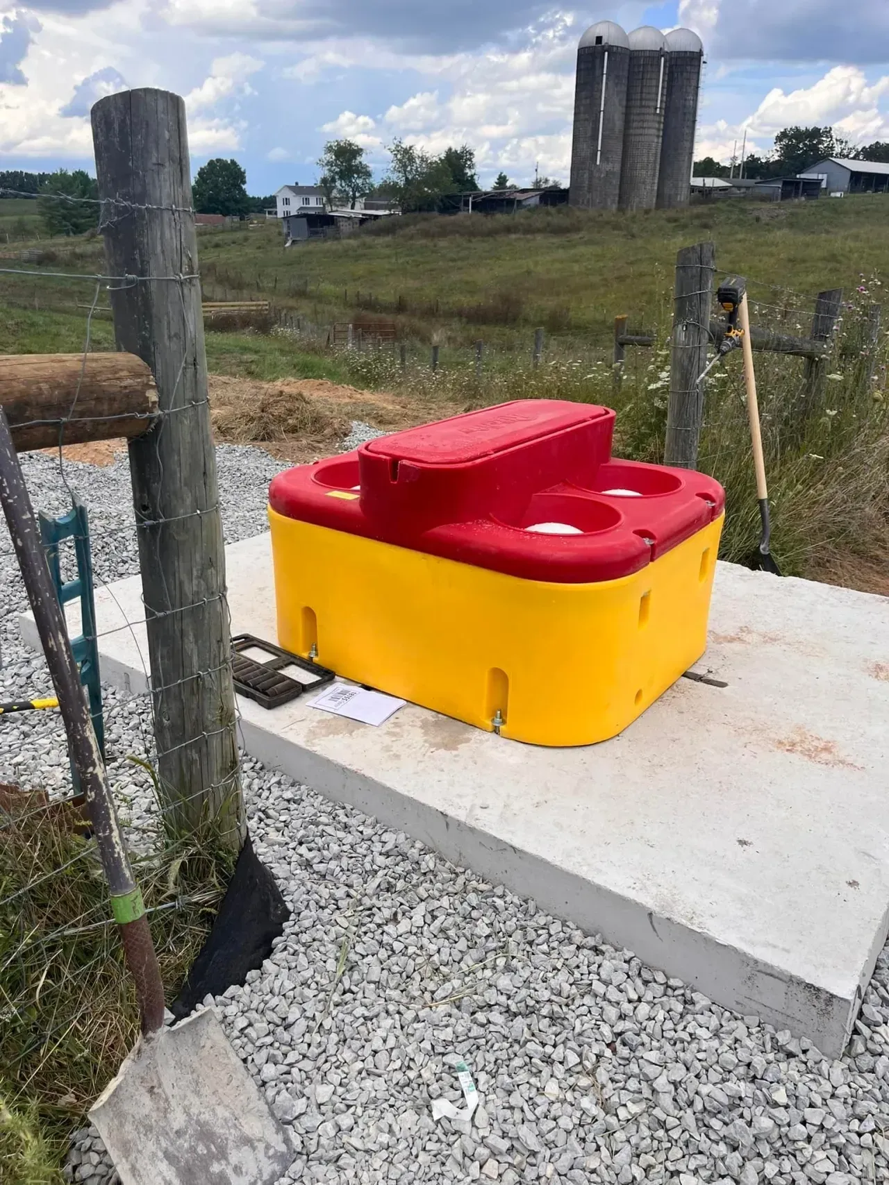 Bright yellow and red utility box on a concrete pad beside a gravel path and fence posts outdoors