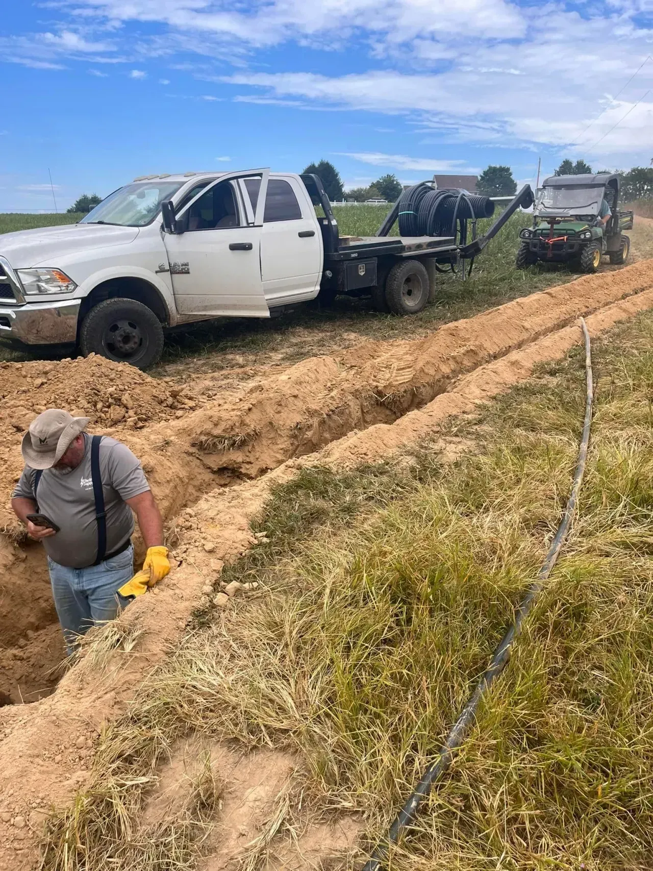 Two white trucks on a muddy dirt road, with a person working in the foreground under a blue sky.
