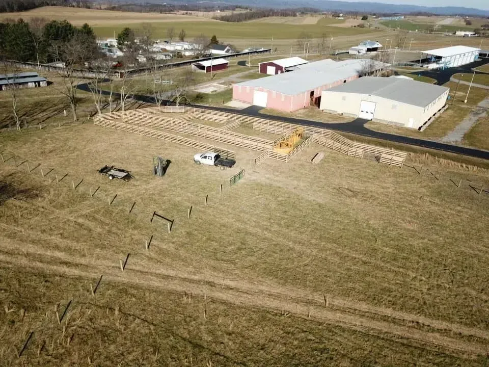 Aerial view of a rural farm field with a white pickup, equipment, and barns near a road.