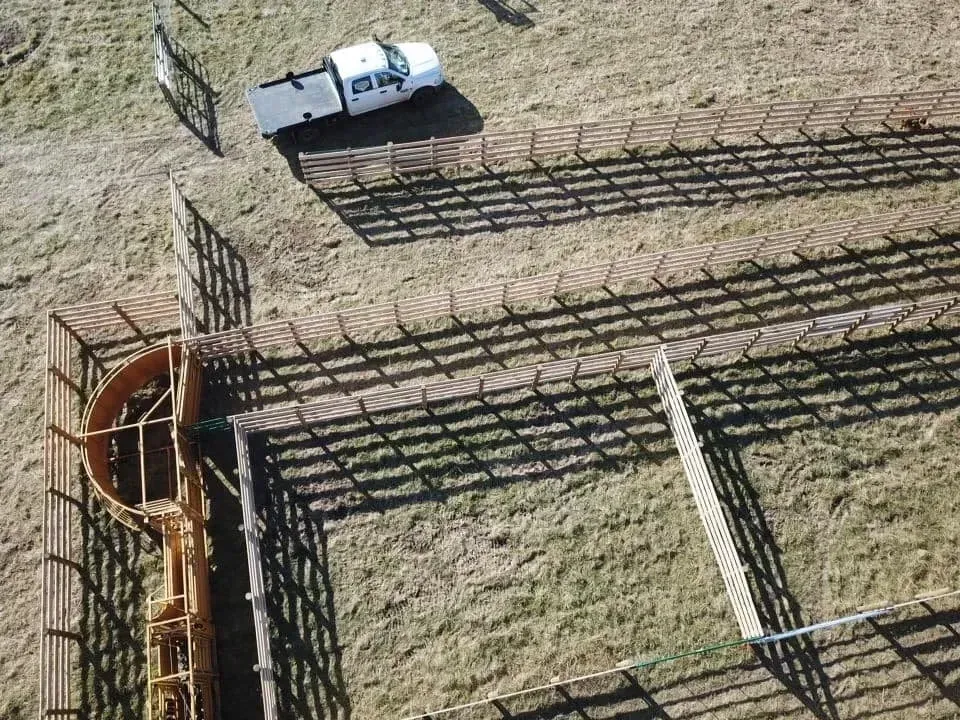 White pickup truck beside long wooden livestock fences in a dry, open ranch field.