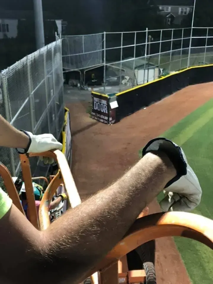 Baseball fan leaning on a rail above the outfield wall at a stadium, with field and fence below.