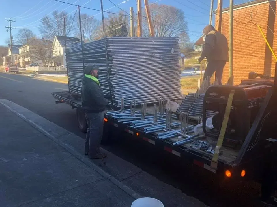 Workers unloading stacked metal panels from a flatbed truck on a residential street