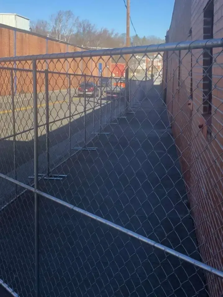 Chain-link gate blocking an alley between brick buildings, with a car parked in the distance.