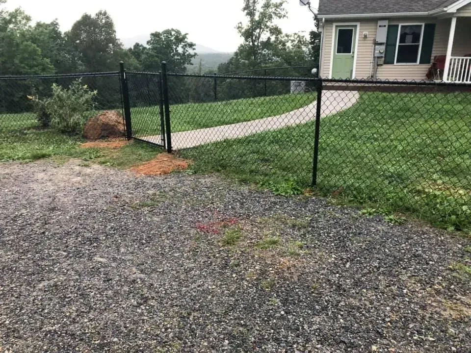 Chain-link fence beside a gravel driveway and curved concrete path leading to a house.