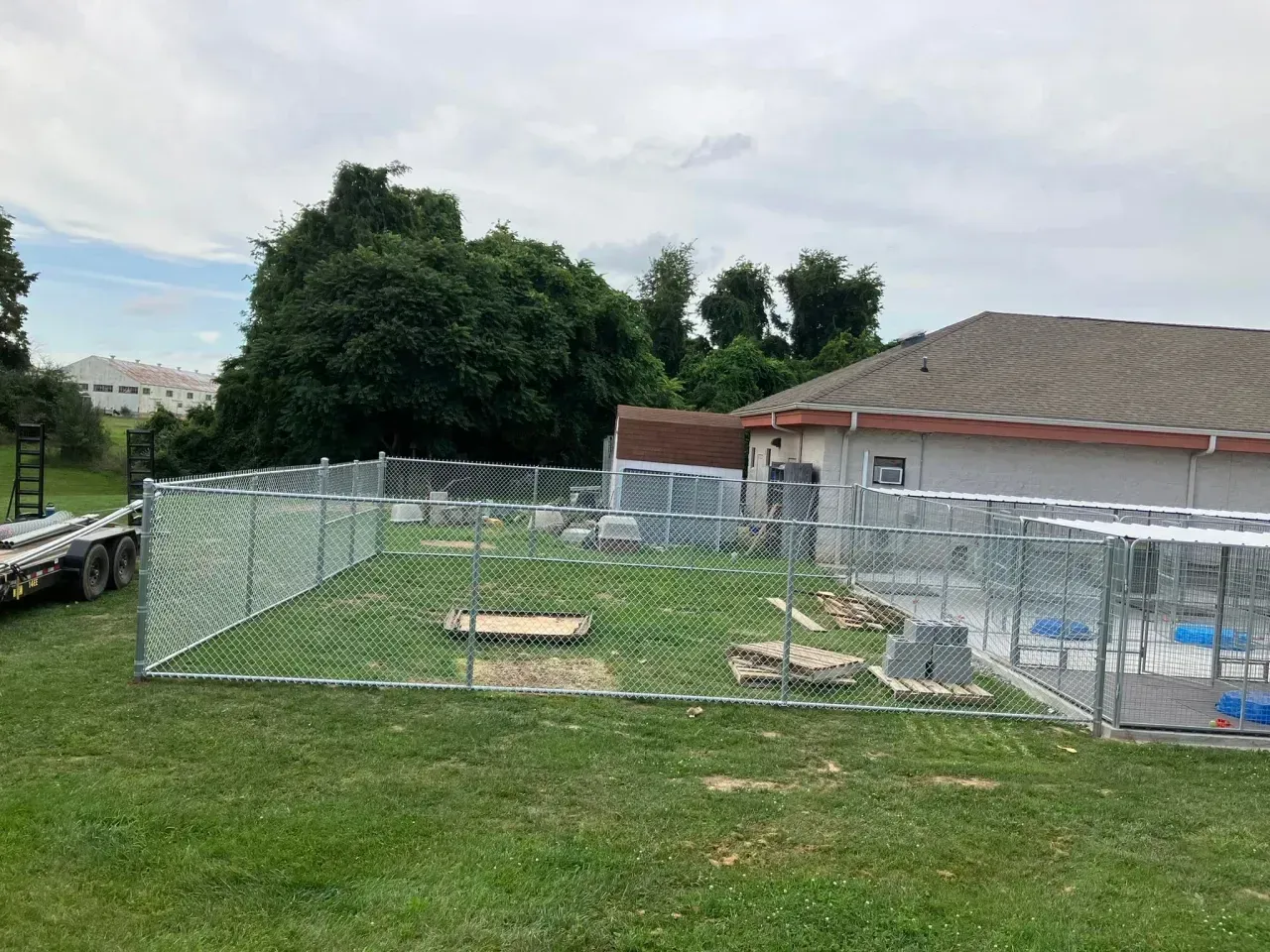 Fenced grassy yard with concrete slabs beside a house under a cloudy sky