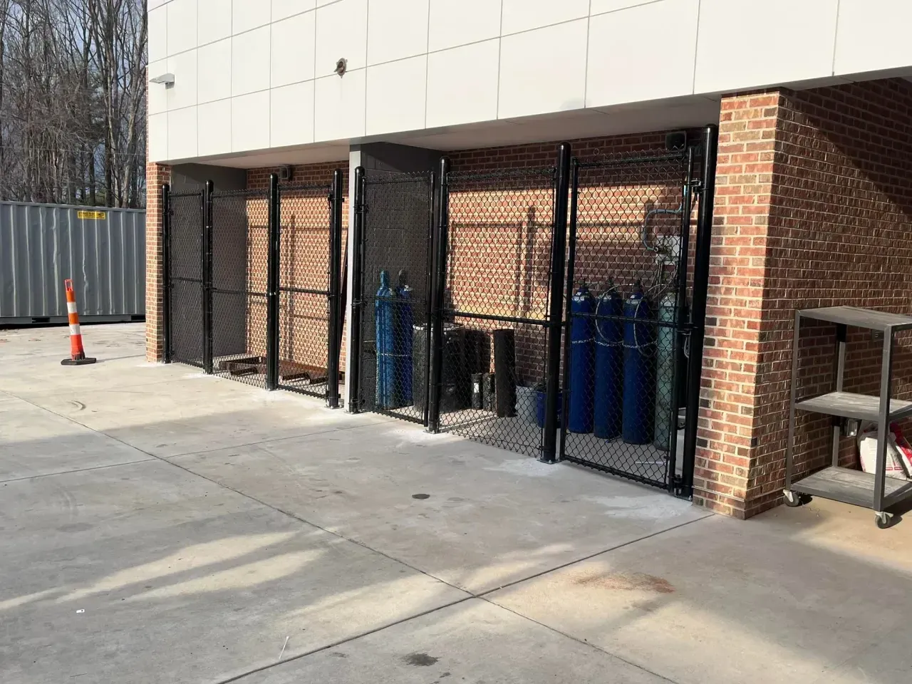 Outdoor service area with chain-link enclosures and blue gas cylinders beside a brick building