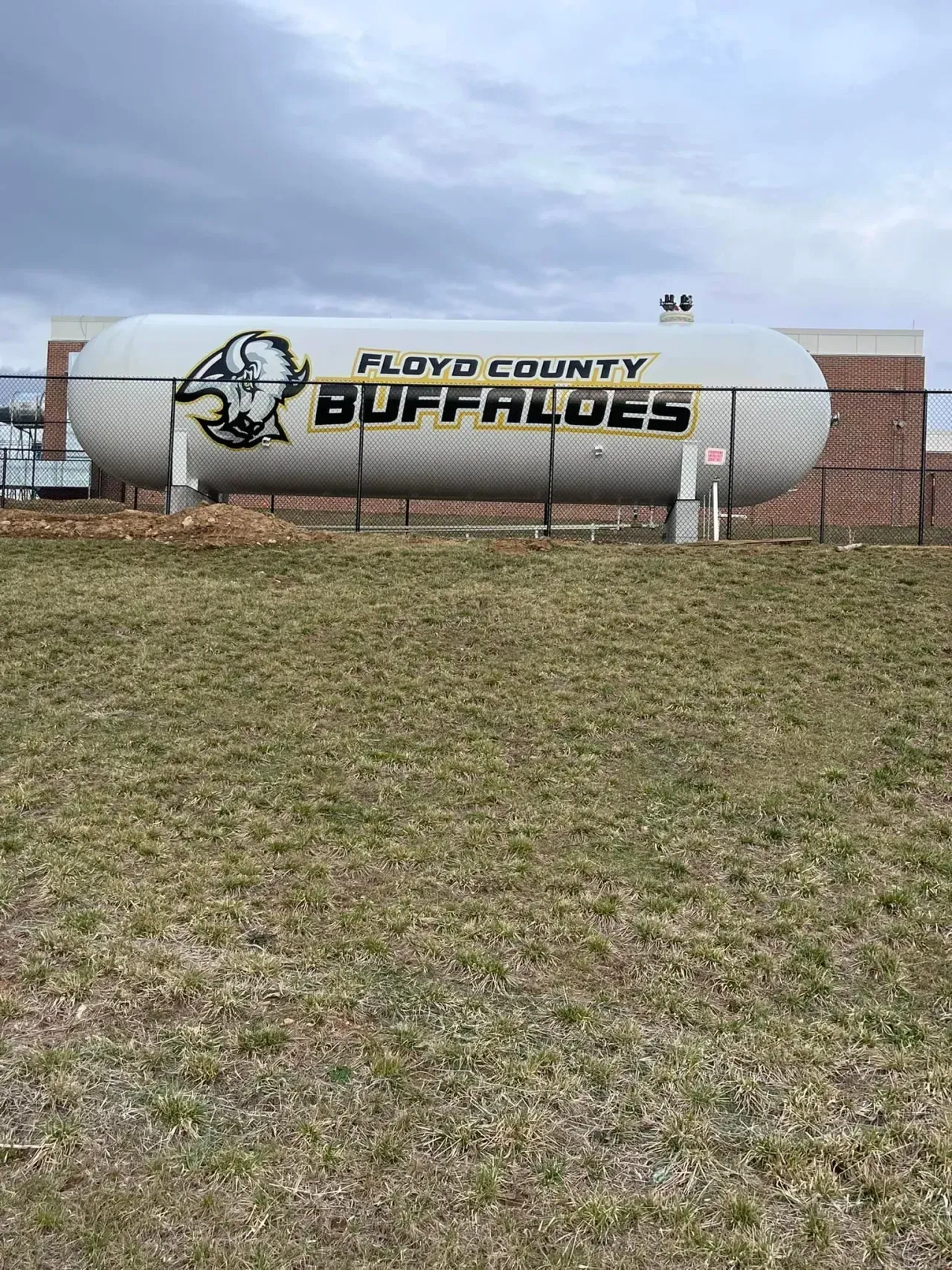 Floyd County Buffaloes sign on a white tank beside a brick wall under a cloudy sky.