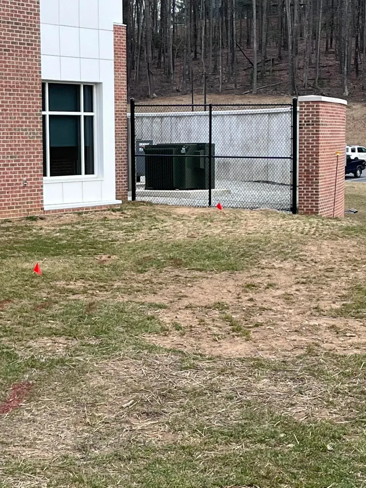 Brick building exterior with a chain-link fenced utility area beside a grassy yard