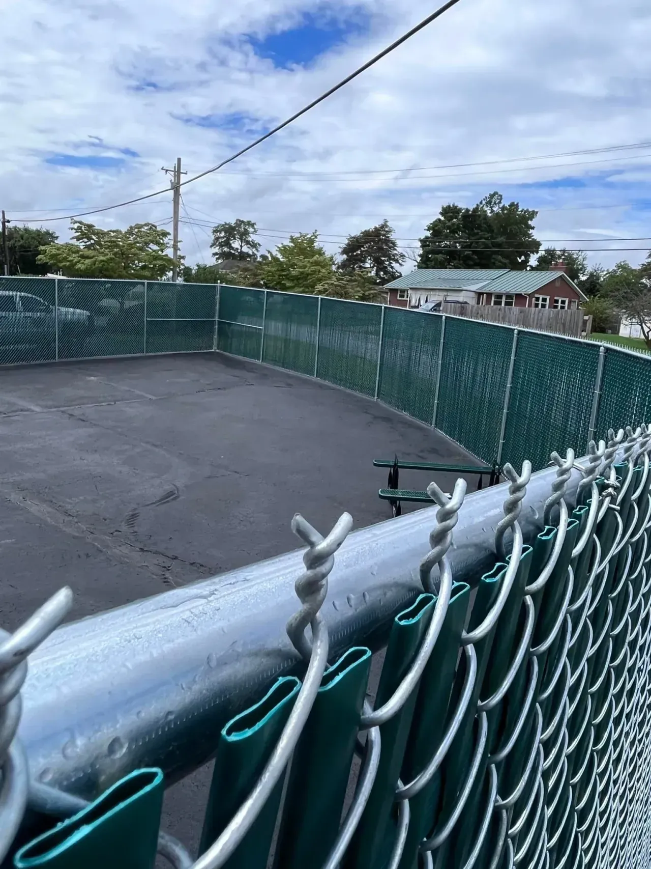 Empty fenced tennis court with green chain-link fence under a cloudy sky
