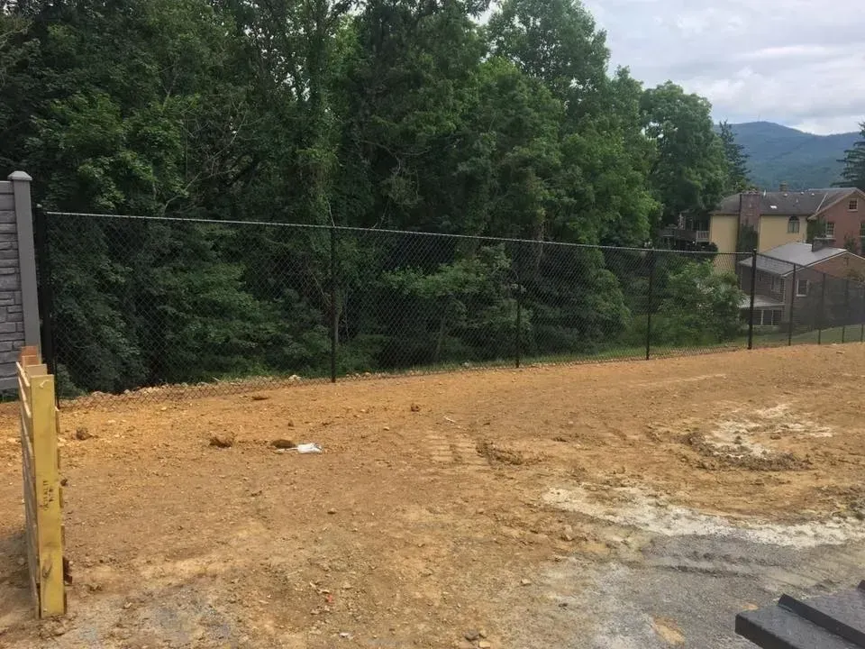 Dirt lot beside a chain-link fence, with trees and hills in the background.