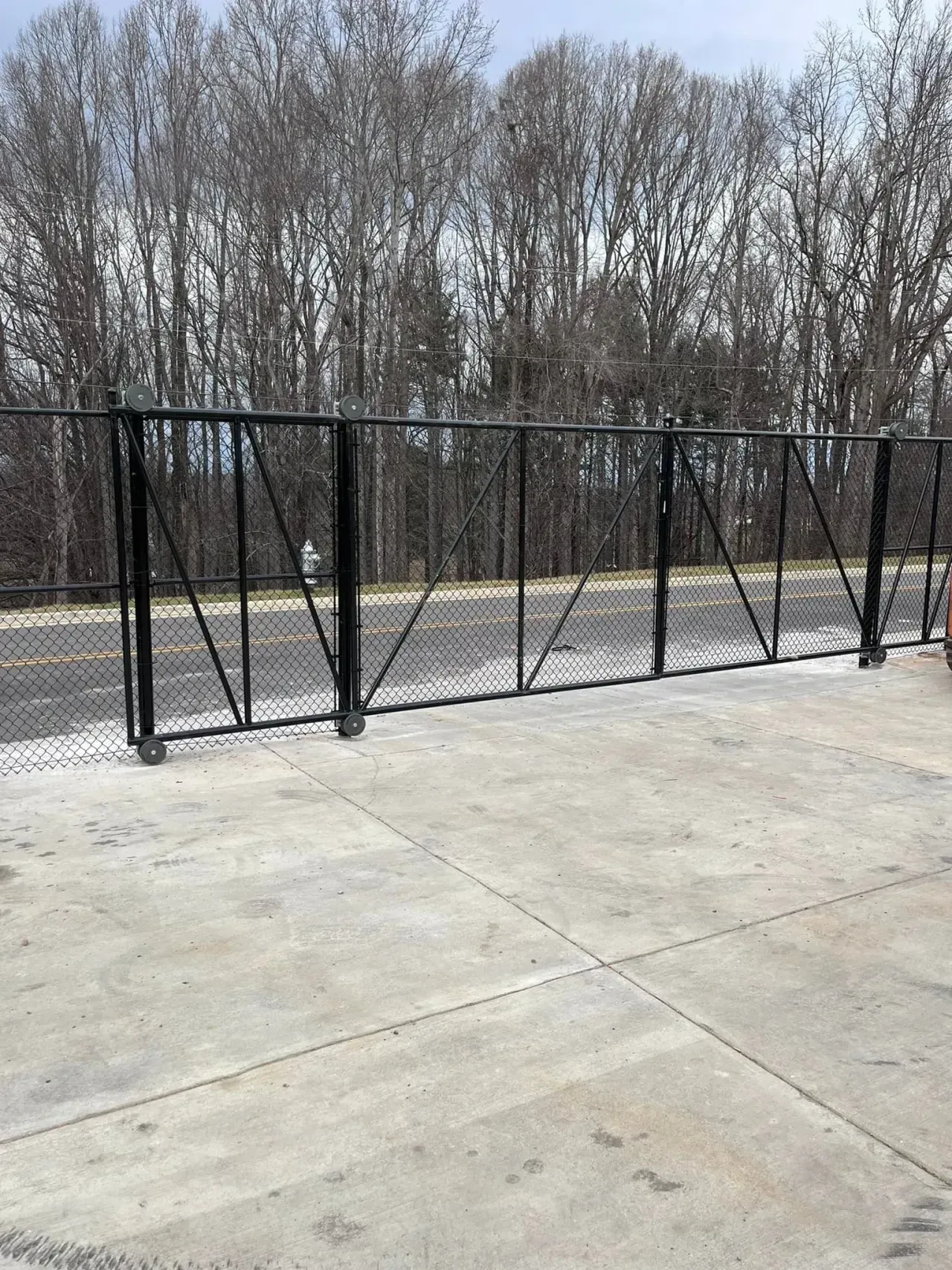 Black metal fence along a concrete lot with leafless trees in the background