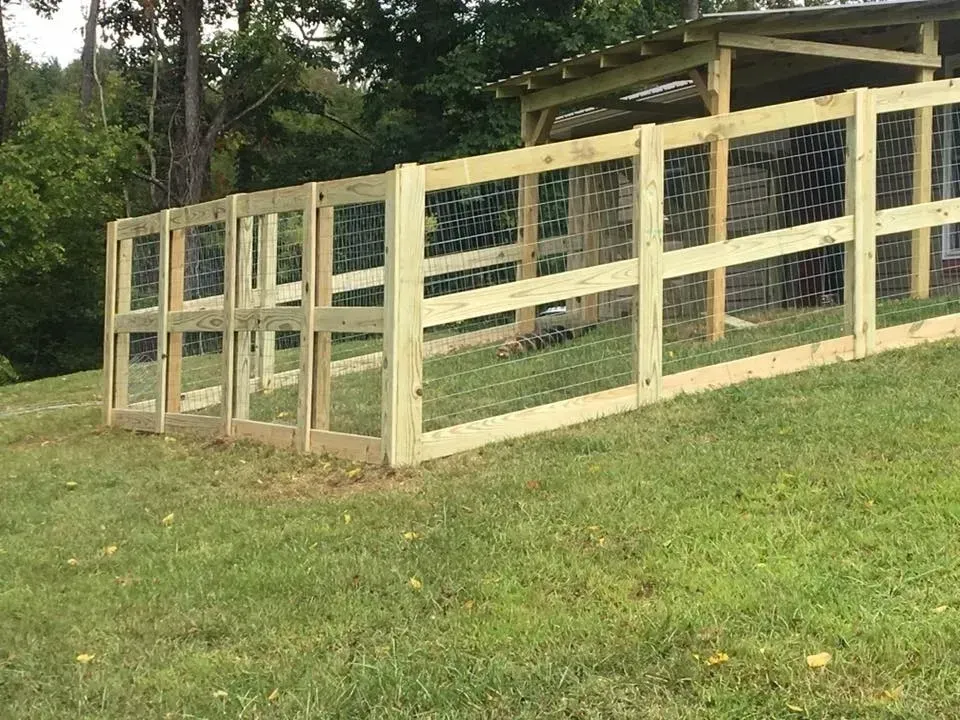 Wooden fenced animal enclosure with a small shelter on a grassy yard