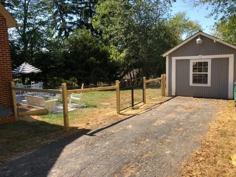 Gravel driveway beside a fenced yard leading to a small gray shed with a white door and window.