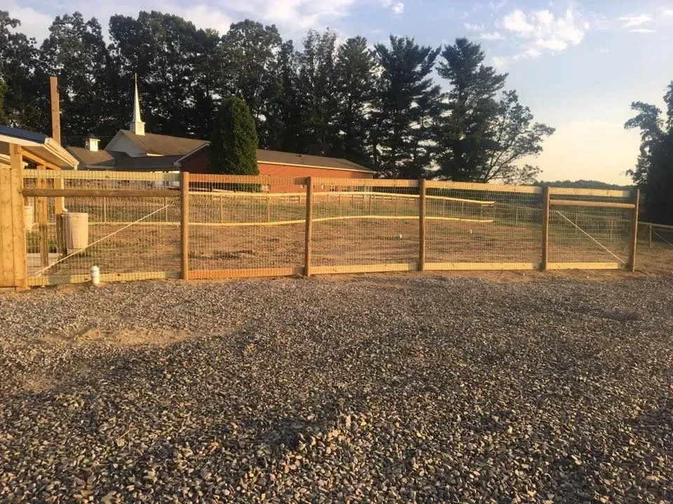 Wooden fenced gravel lot at sunset with trees and a house in the background