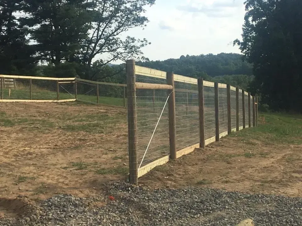Wooden fence along a dirt path on a grassy hillside, with trees and hills in the background