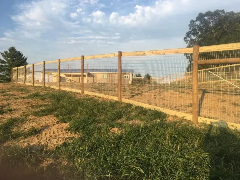 Wooden fence around a grassy dirt lot under a partly cloudy sky