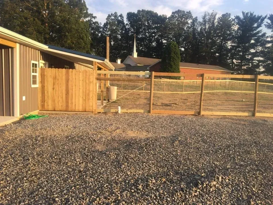 Gravel yard beside a wooden shed and fence, with trees and houses in the background.