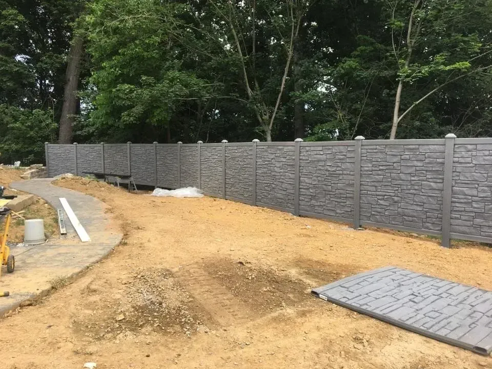 Curved dirt driveway under construction beside a gray block wall and trees