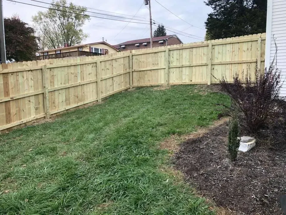 Backyard with a new wooden fence, sloped grassy lawn, and a mulched planting bed on the right