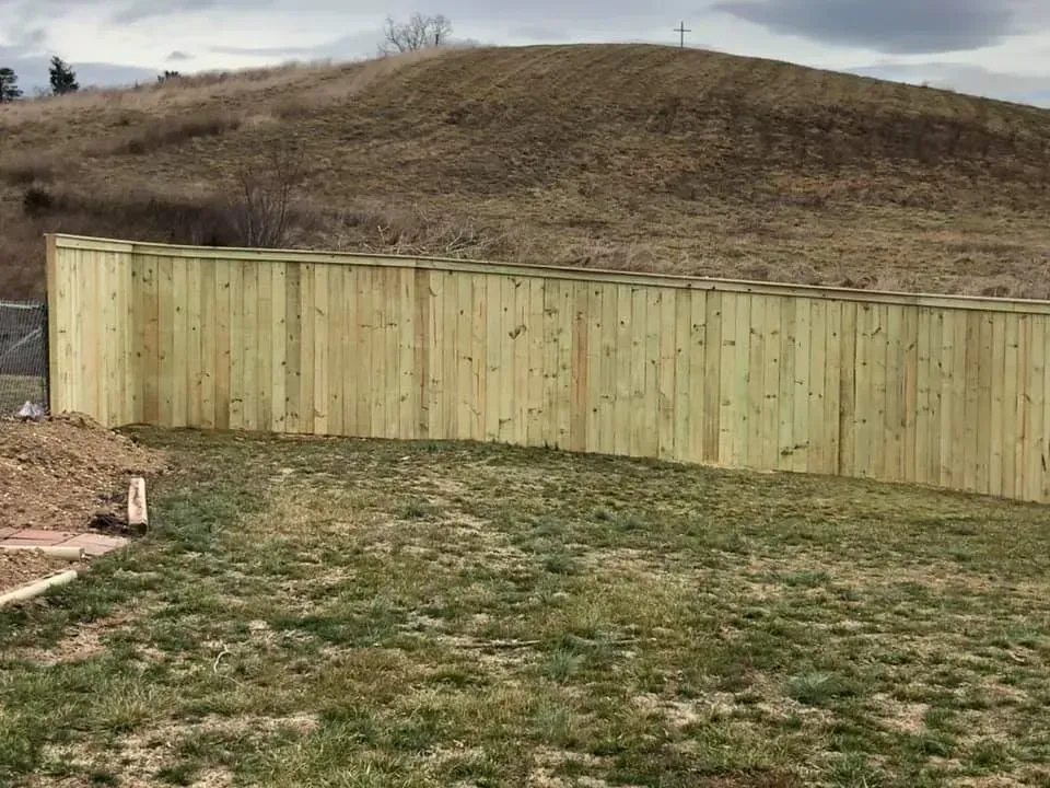 Wooden privacy fence in a grassy yard with a brown hill behind it under a cloudy sky