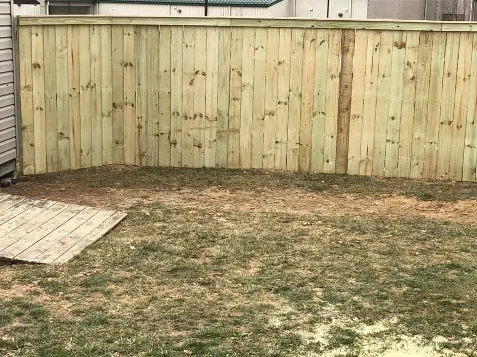 Small backyard with patchy grass, a wooden privacy fence, and a paved corner patio.