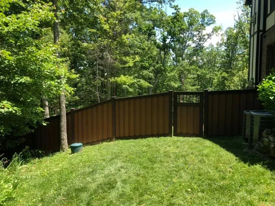 Grassy backyard with a curved wooden fence, trees, and a building on the right
