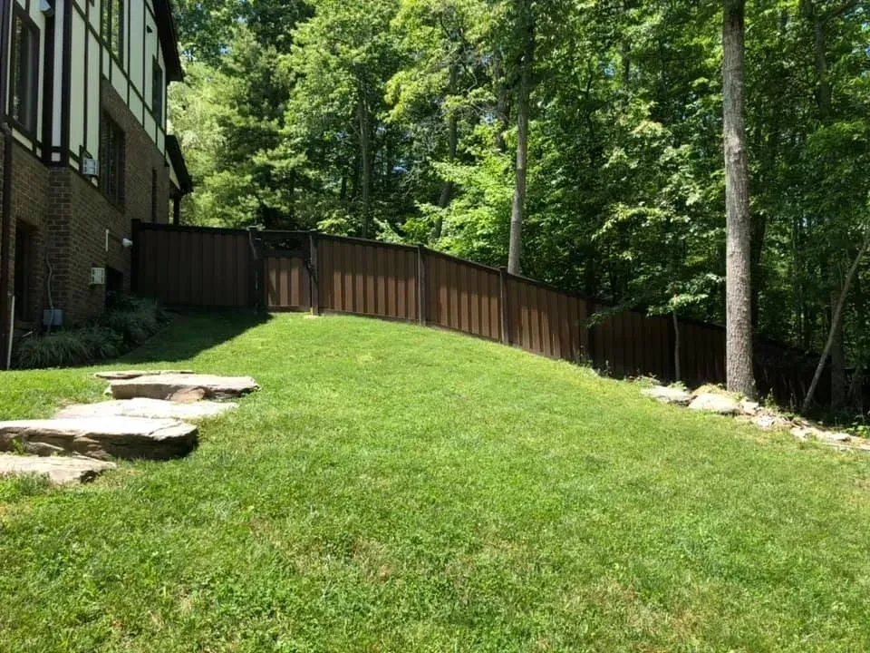 Backyard lawn with stone steps, wooden fence, and tall trees beside a house