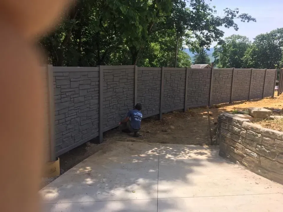 Backyard concrete patio beside a gray stone retaining wall, with a person kneeling near the wall.