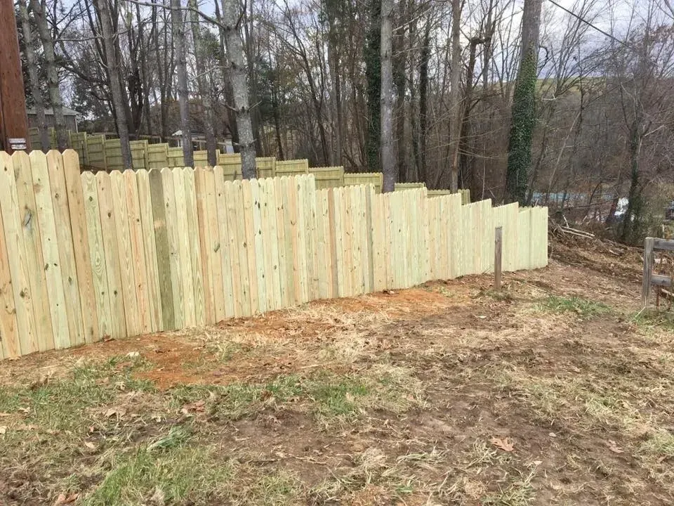 New wooden privacy fence along a wooded backyard slope