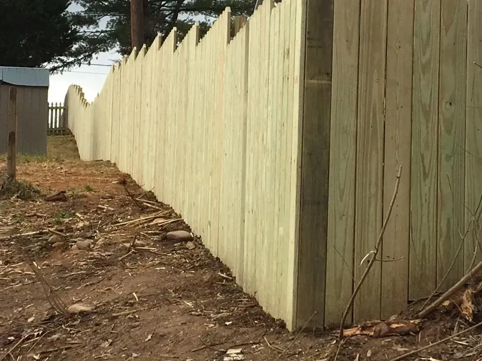 Long pale wooden fence along a dirt path beside a tree-lined yard