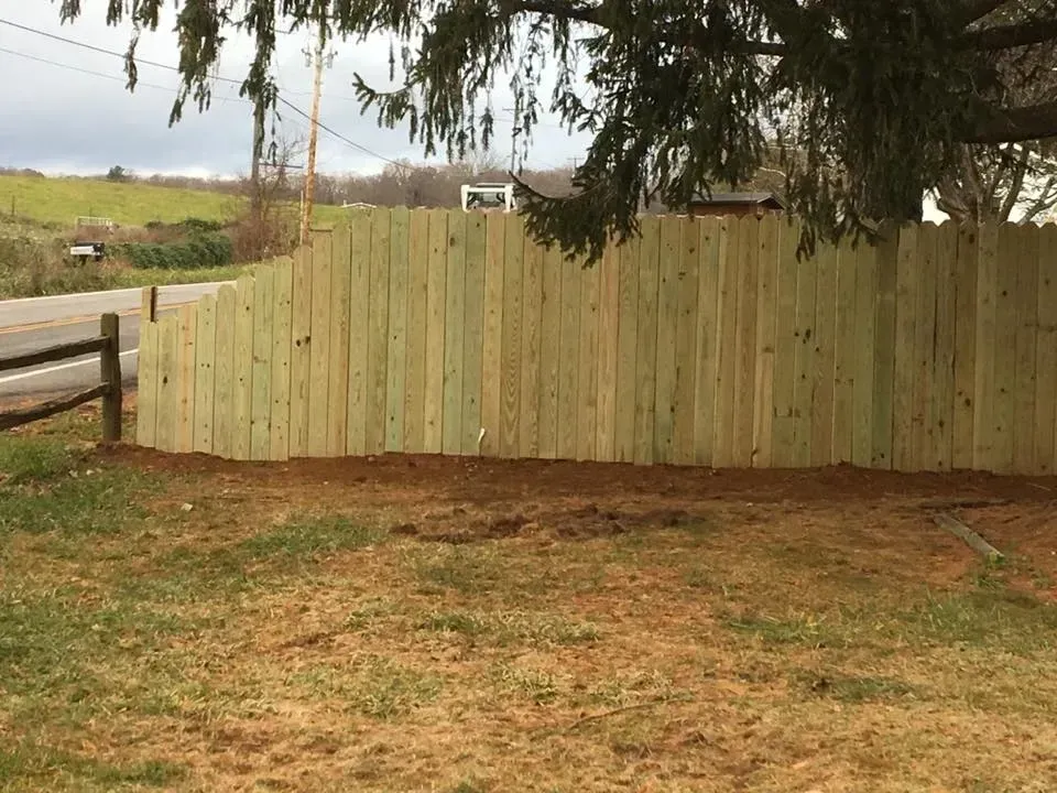 Wooden fence across a grassy field with trees overhead and hills in the background