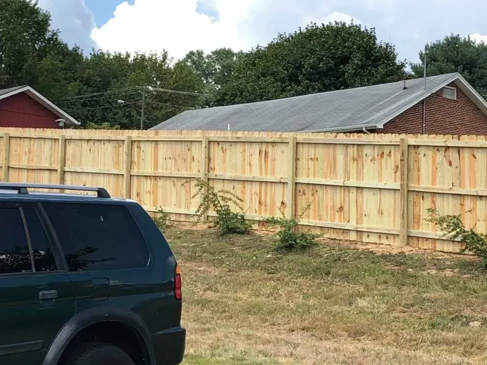 Wooden privacy fence behind a dark SUV in a grassy backyard under a partly cloudy sky