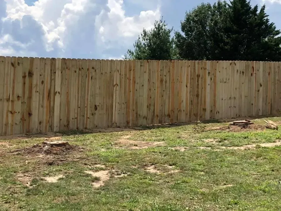 Tall wooden privacy fence bordering a patchy grassy yard under a partly cloudy sky