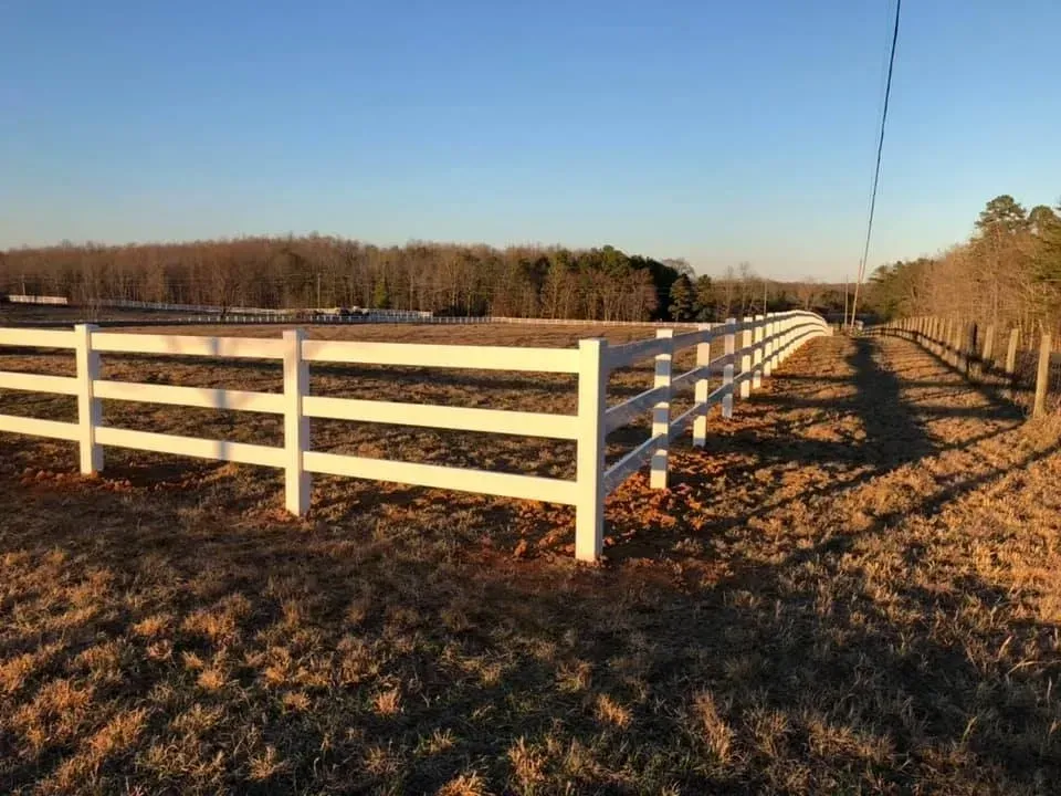 White fence along a dirt path in a rural field at sunset