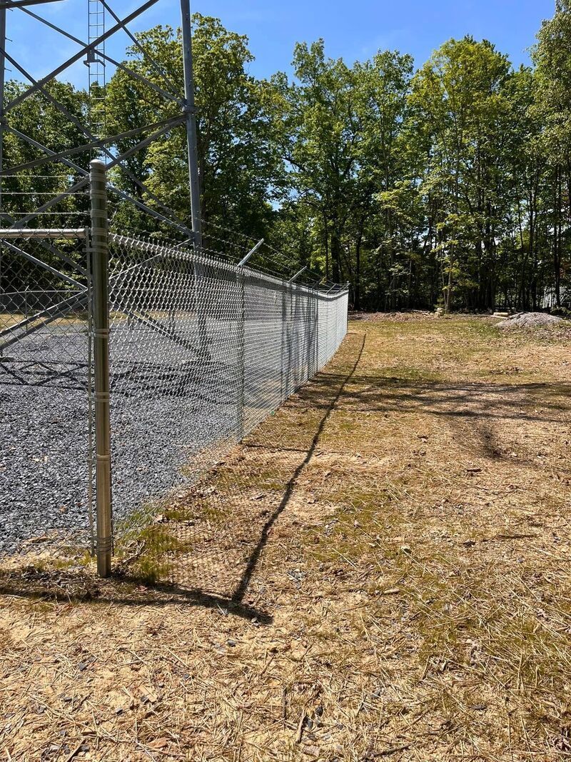 Chain-link fence beside a gravel path under trees on a sunny day