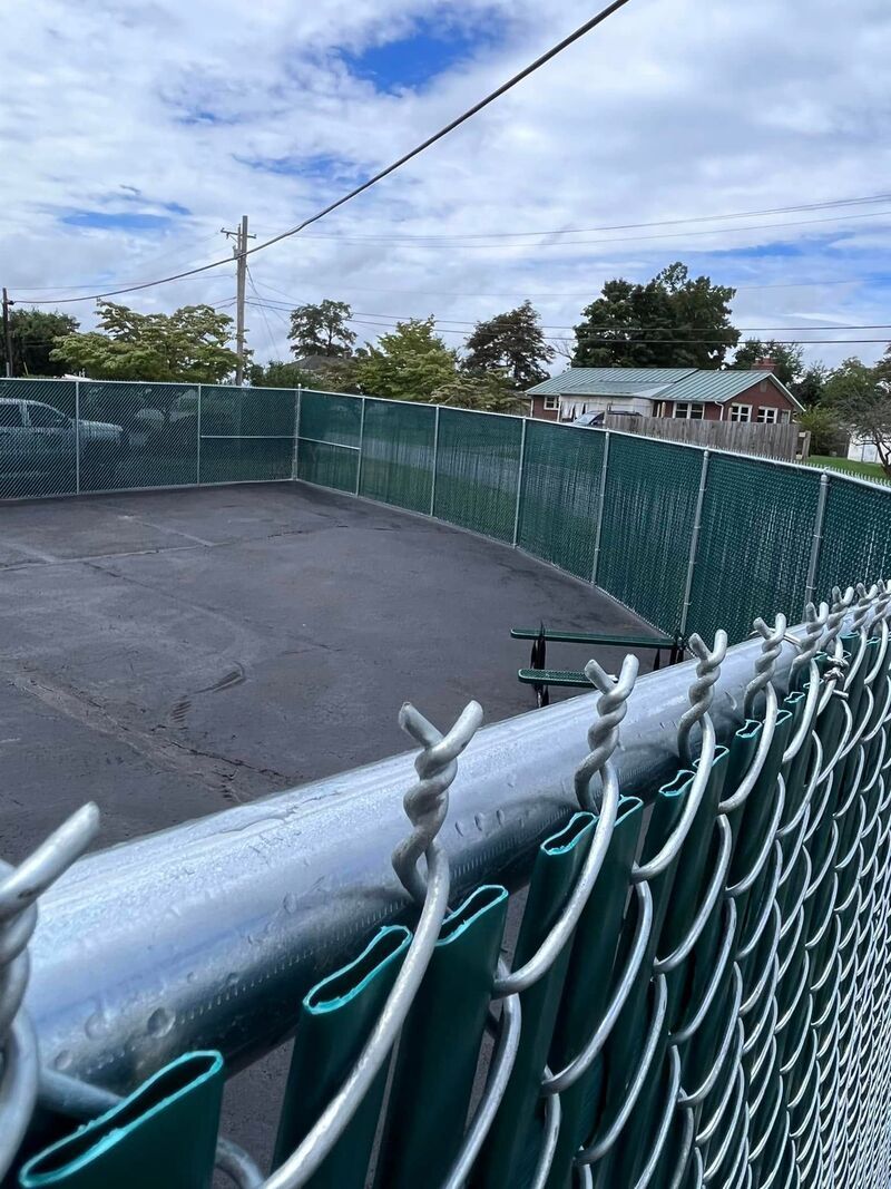 Empty fenced court with green chain-link fence under a cloudy sky