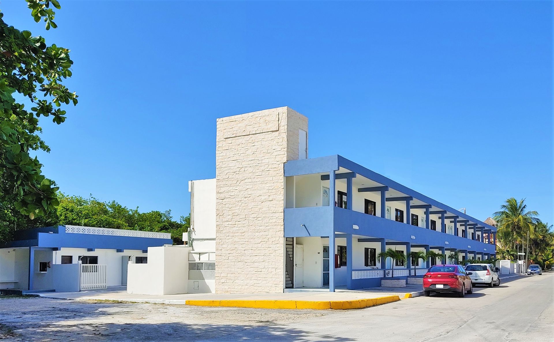 Un edificio azul y blanco con coches aparcados delante.