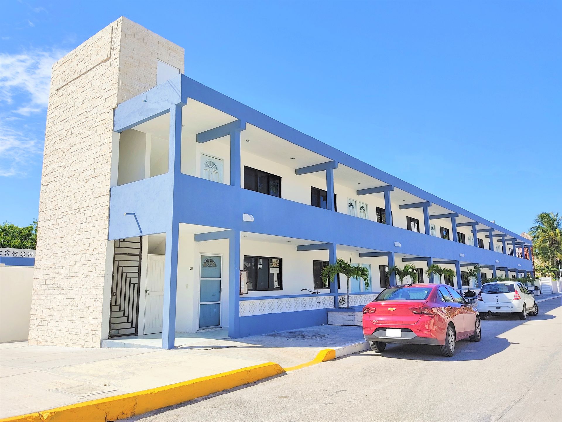 Un edificio azul y blanco con un coche rojo aparcado delante.