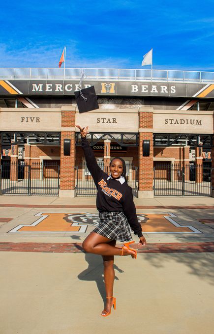 Woman in black dress posing with one leg raised outside Mersh Bears stadium entrance under a blue sky