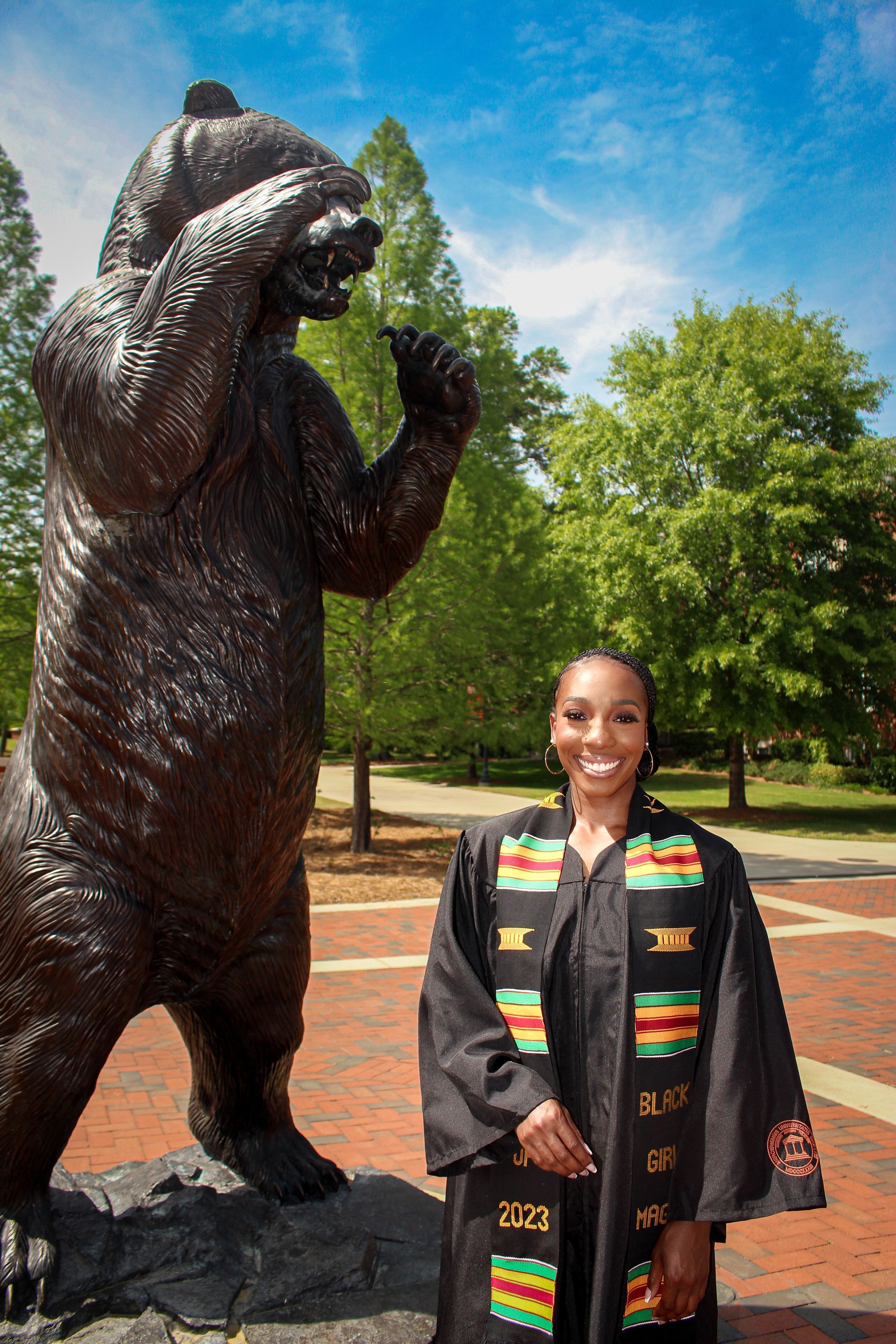 Woman standing beside a large bear statue in a park on a sunny day