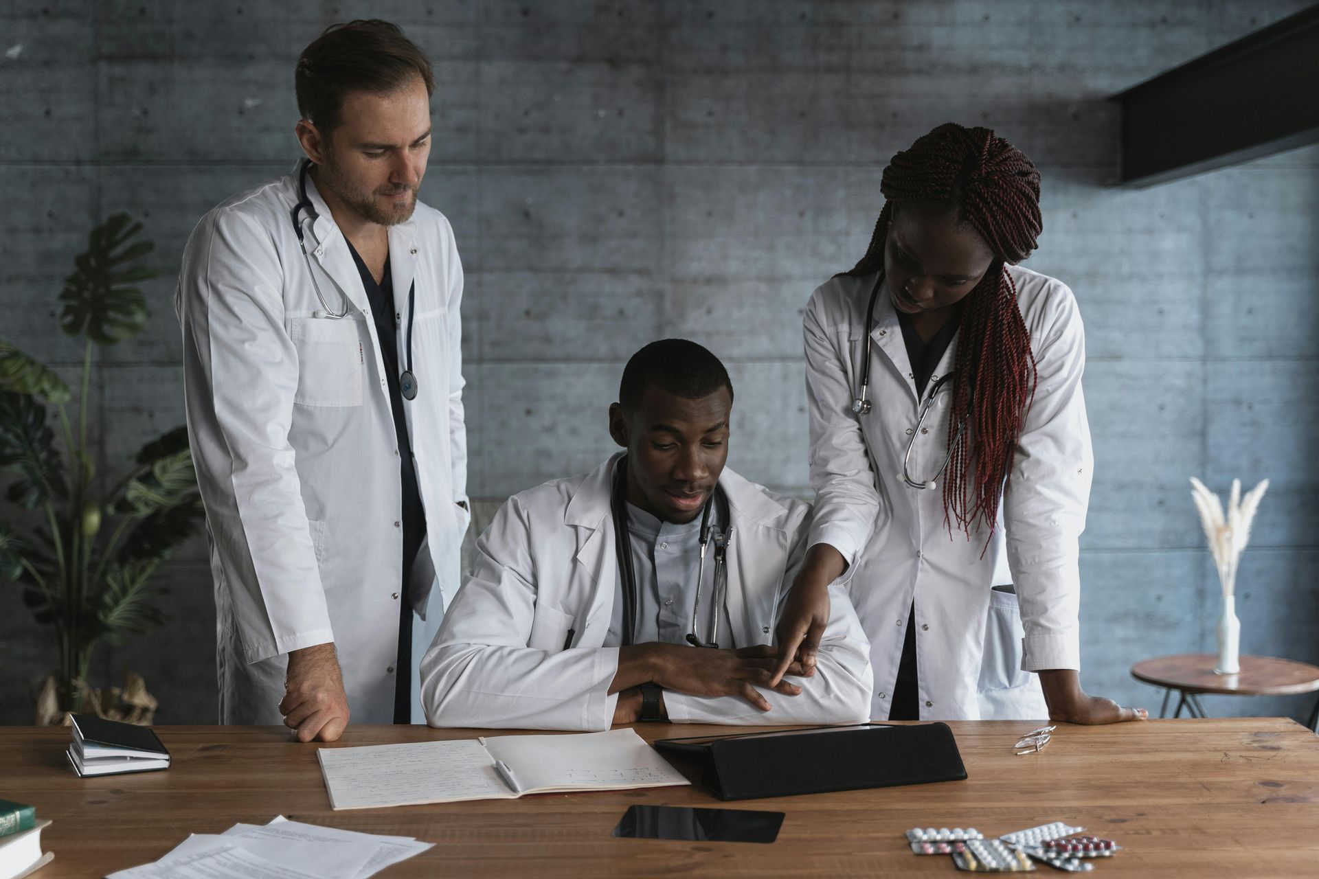 Three medical staff in white coats reviewing documents at a wooden table in a clinic office