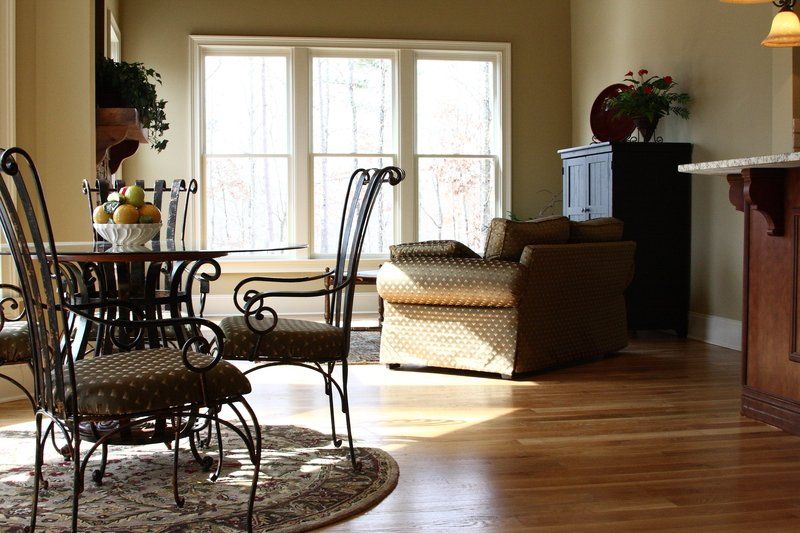 Sunlit living room with wicker chairs, round table, sofa, and hardwood floor near French doors