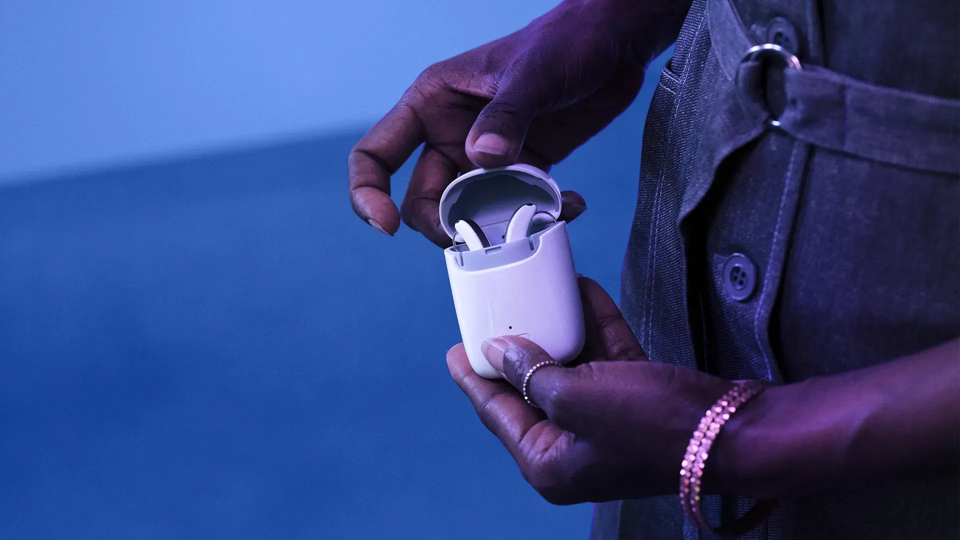 Hands holding open white case with two earbuds; blue background.
