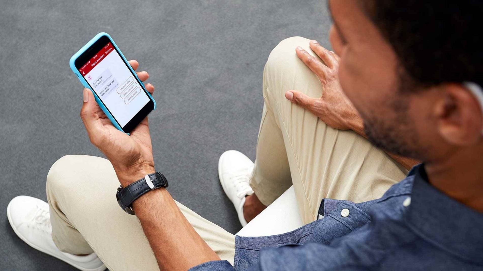 Person seated looking at smartphone screen, possibly monitoring health data, with a hearing aid visible.
