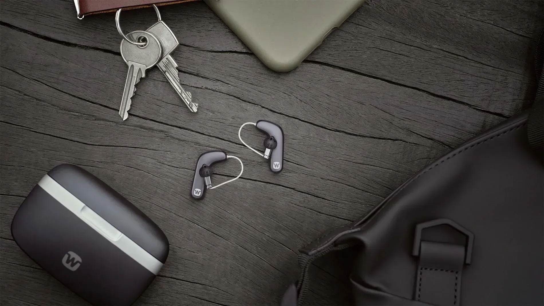 Earbuds, keys, phone, and bag on a dark wood surface.