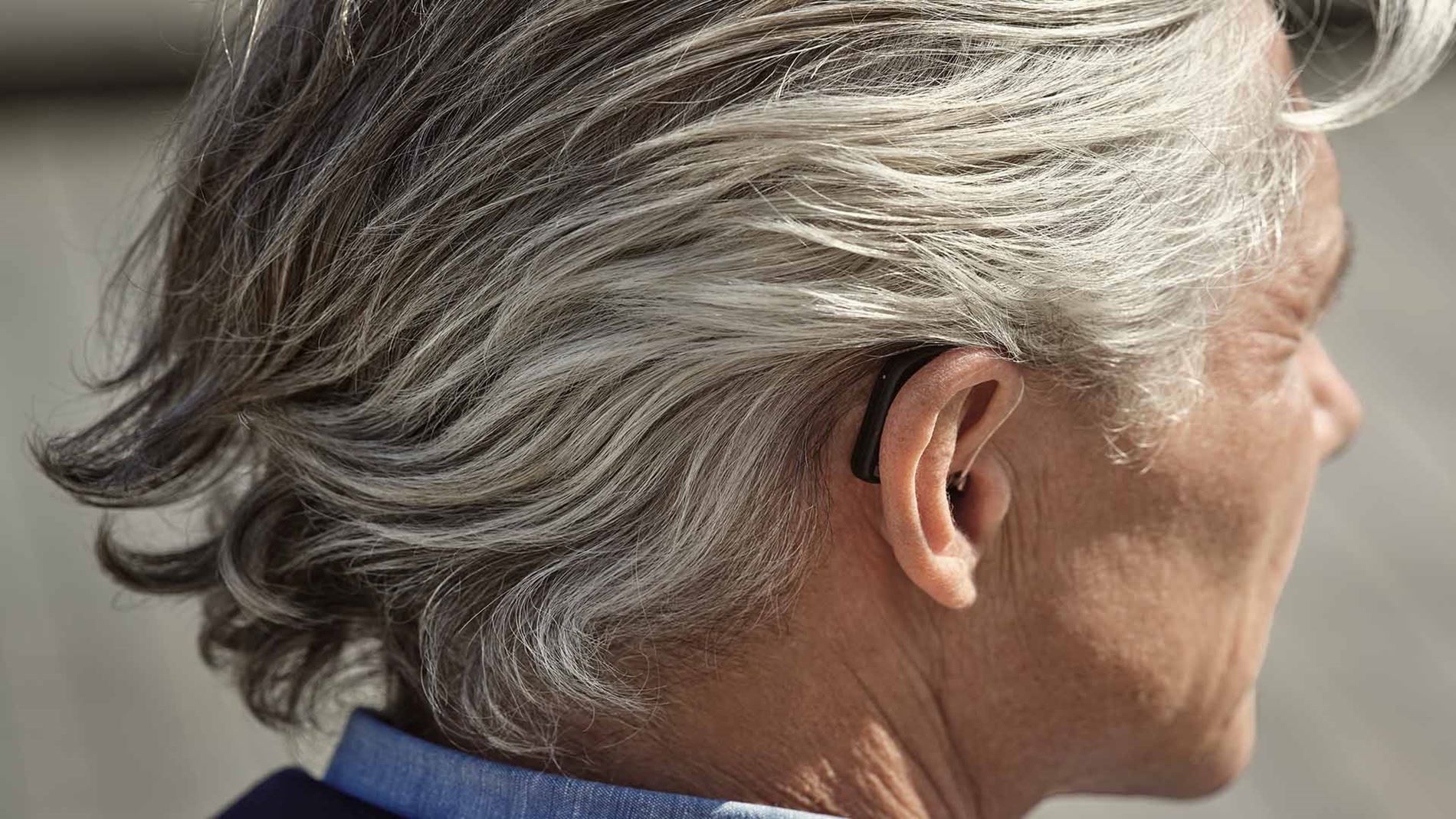 Man with gray hair, wearing a hearing aid behind his right ear.